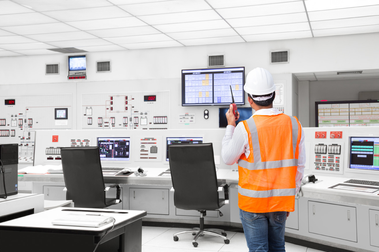 Engineer wearing hard hat and safety vest, using radio to communicate with power plant operators.