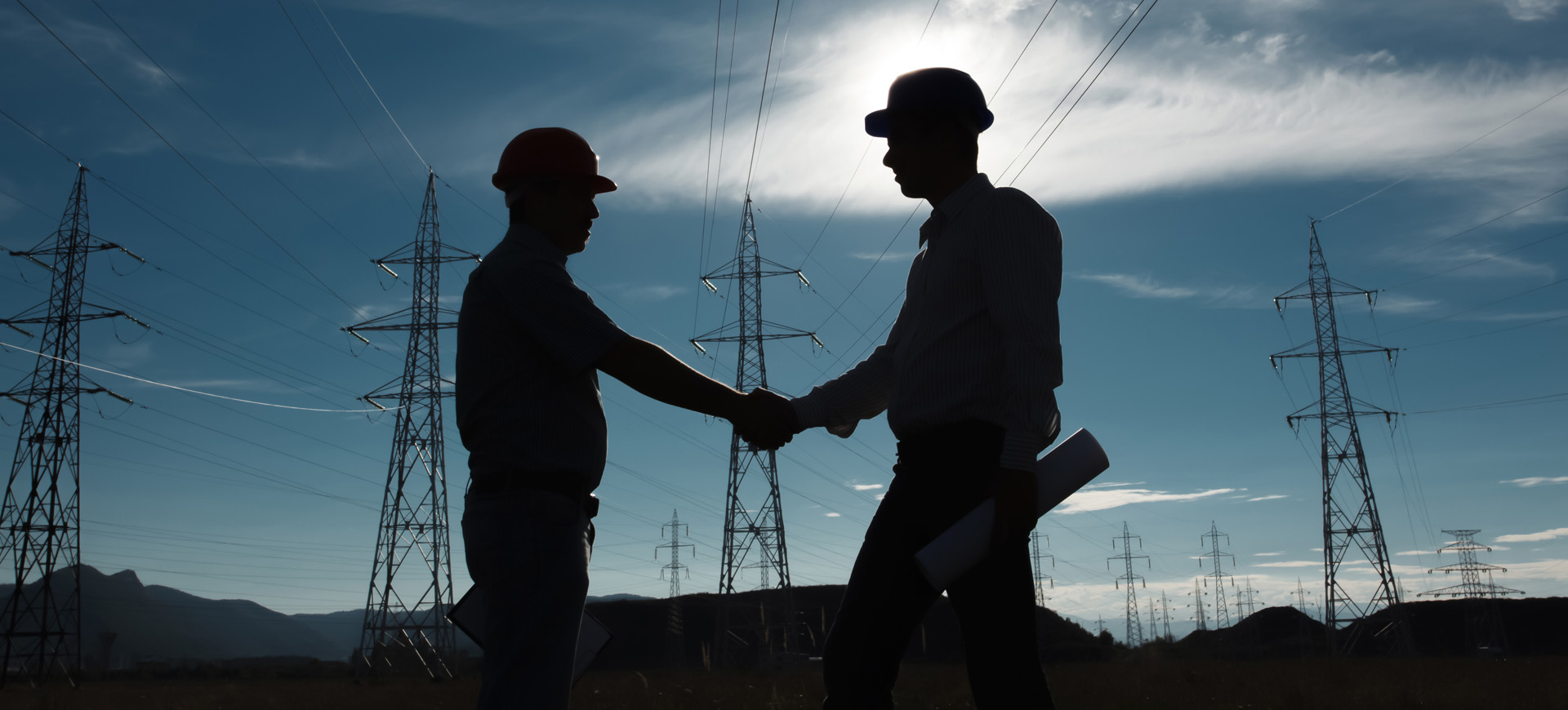 Silhouette of Engineers Shaking Hands in front of High Voltage Power Lines