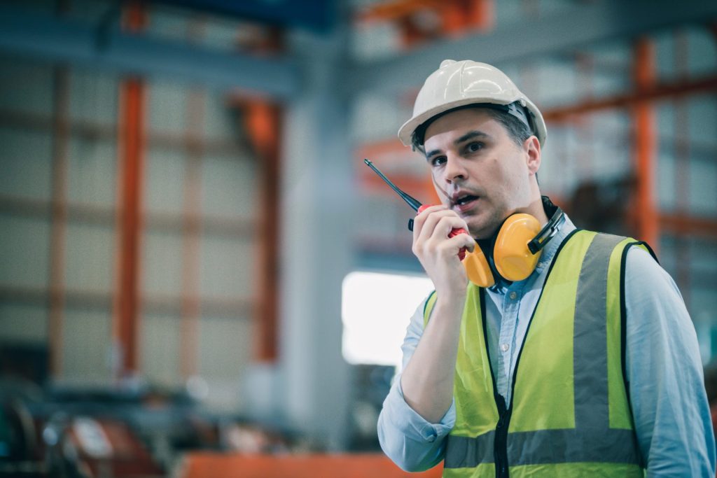 A man wearing a hard hat and safety vest talking on a walkie talkie